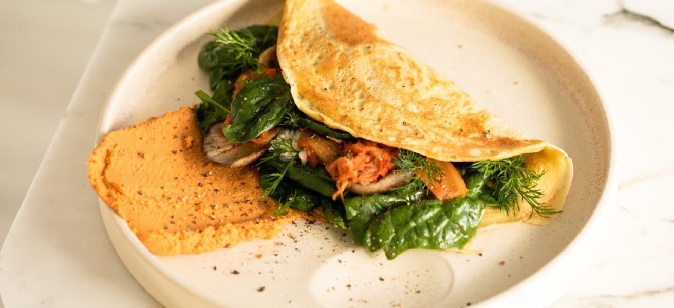 folded omelette with cheese, diced vegetables, cooked meats and herbs in the center on a white plate